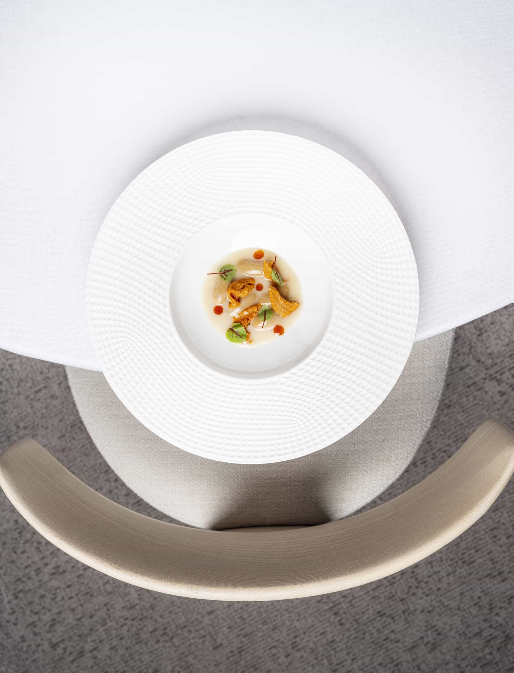 Vista cenital de plato de degustación y silla ergonómica de madera maciza de Andreu World en el restaurante Clos de Madrid.